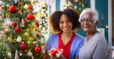 Home Care and the Heartwarming Spirit of Christmas. Picture of a young black female and an older black female standing beside a Christmas tree.